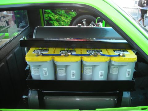 1998 Ford Crown Victoria - Four yellow-cased batteries sit in a custom rack inside the bed of a bright green show vehicle.