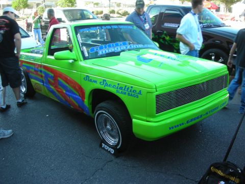 1998 Ford Crown Victoria - lime-green mini truck with airbag graphics and chrome wheels sits lowered at an outdoor car show.