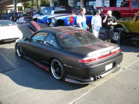 1998 Ford Crown Victoria - Rear view of a lowered matte-black coupe with red pinstripe accents and black wheels at a car show.