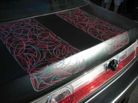 1998 Ford Crown Victoria - Intricate red and silver pinstriped artwork covers the trunk lid of a dark-colored car near the taillight.