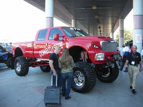 1998 Ford Crown Victoria - heavily lifted red crew-cab pickup on oversized tires towers over onlookers at an indoor display.