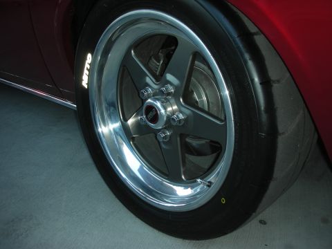 1998 Ford Crown Victoria - Close-up of a polished five-spoke wheel and Nitto tire mounted under the red fender of a show car.