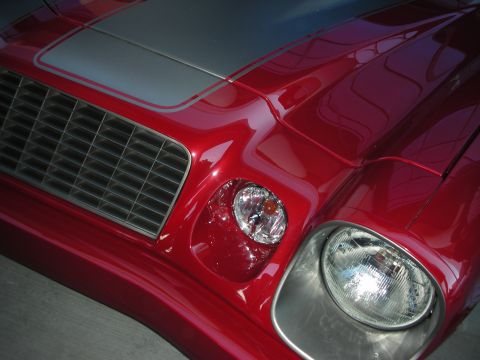 1998 Ford Crown Victoria - Close-up of a red Camaro's front corner showing the round headlight, slotted grille and silver hood stripe.