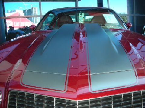 1998 Ford Crown Victoria - Front-on view of a red muscle car with twin silver hood stripes and chrome grille at an indoor show.
