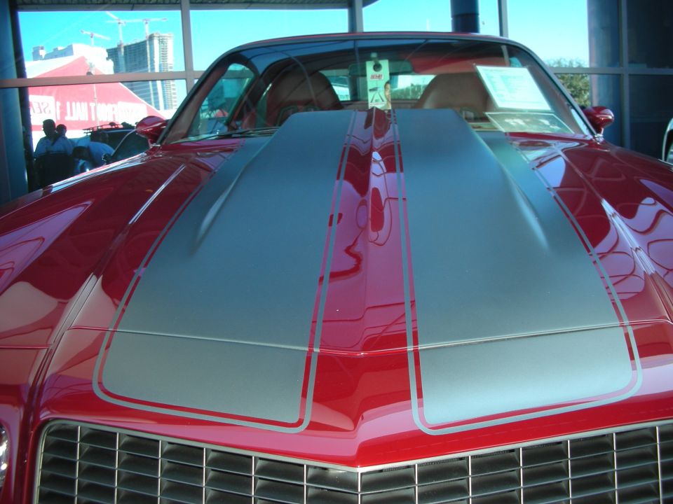 Front view of a red muscle car with silver dual hood stripes and grille