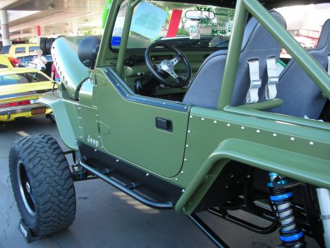 1998 Ford Crown Victoria - Driver-side view of an olive-green Jeep with riveted aluminum body panels, exposed roll cage, racing seats and blue coilover shocks.