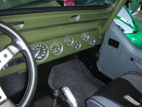 1998 Ford Crown Victoria - Interior of an olive-green custom vehicle showing an aftermarket gauge cluster, steering wheel and chrome floor-mounted shifter on carpet.