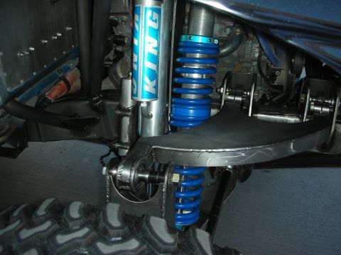 1998 Ford Crown Victoria - Close-up of a blue King coilover shock and reservoir mounted to a fabricated tubular suspension arm beneath an off-road vehicle.