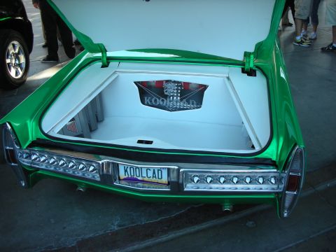 1998 Ford Crown Victoria - Open trunk of a green custom Cadillac with a white-upholstered boot, crest emblem and yellow KOOLCAD license plate.