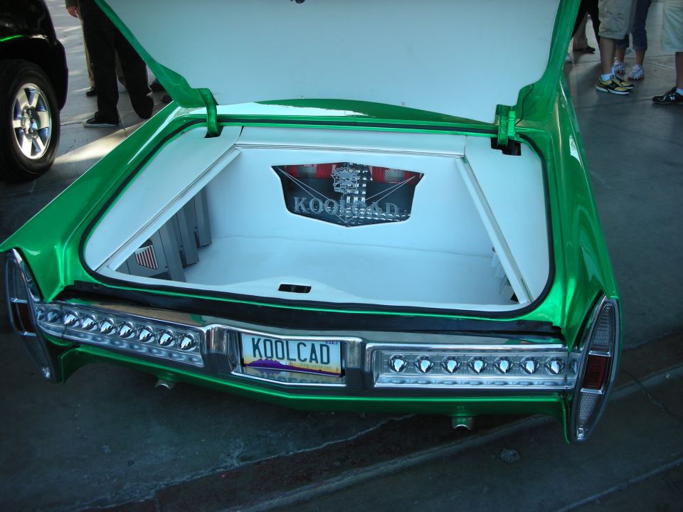 Open trunk of green Cadillac with KOOLCAD plate and white-lined boot