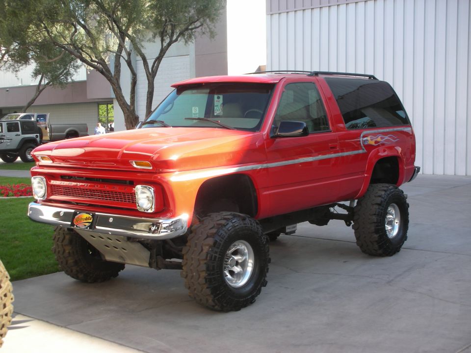 Red lifted two-door Chevrolet SUV on large mud tires parked outdoors