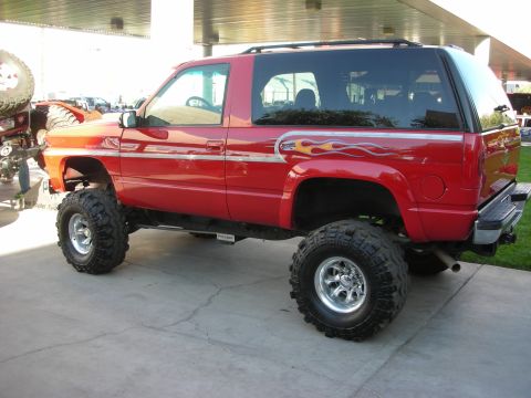 1998 Ford Crown Victoria - Rear quarter view of a red lifted two-door SUV with flame side graphics, raised suspension and oversized mud tires under a canopy.
