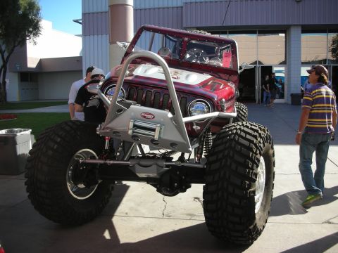 1998 Ford Crown Victoria - Front view of a maroon caged Jeep-bodied rock buggy on huge tires with a fabricated winch bumper, displayed on pavement.