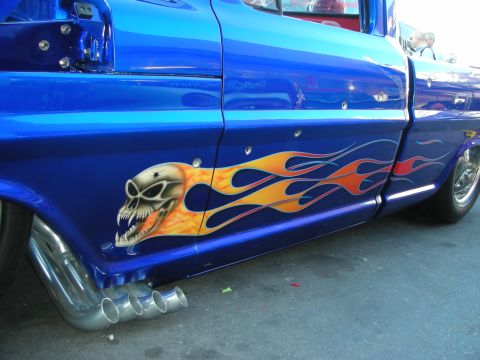 1998 Ford Crown Victoria - Side detail of a blue custom pickup featuring an airbrushed flaming skull, orange flame graphics and chrome side-exit exhaust tips.
