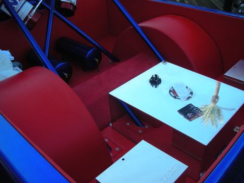 1998 Ford Crown Victoria - Stripped custom interior with red and blue painted panels, an air tank, roll bar and a brochure resting on a white surface.