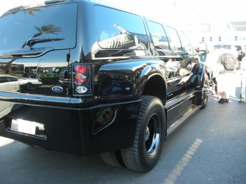 1998 Ford Crown Victoria - Rear three-quarter view of a glossy black Ford dual-rear-wheel crew-cab SUV conversion parked on pavement at an outdoor event.