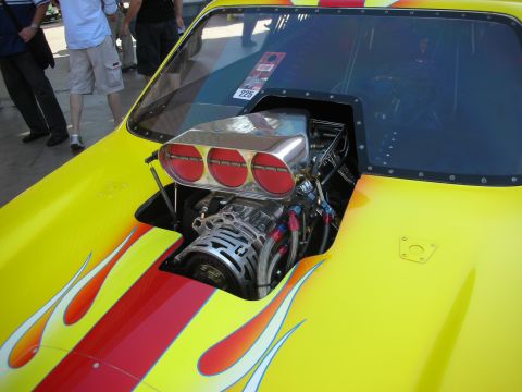 1998 Ford Crown Victoria - polished supercharger and three-port scoop sit atop the exposed engine of a yellow flame-painted drag car cockpit.