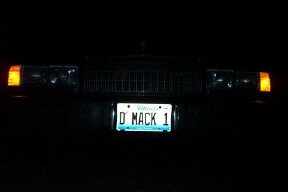 1990 Mercury Grand Marquis - The front of a car is visible at night, illuminated by its headlights and the license plate D MACK 1.
