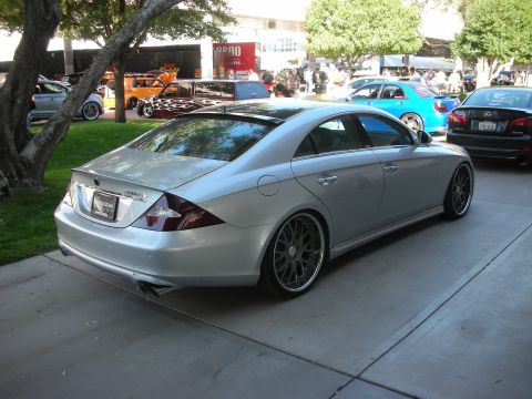 1998 Ford Crown Victoria - lowered silver Mercedes-Benz CLS four-door coupe on dark multi-spoke wheels, parked at an outdoor car show.
