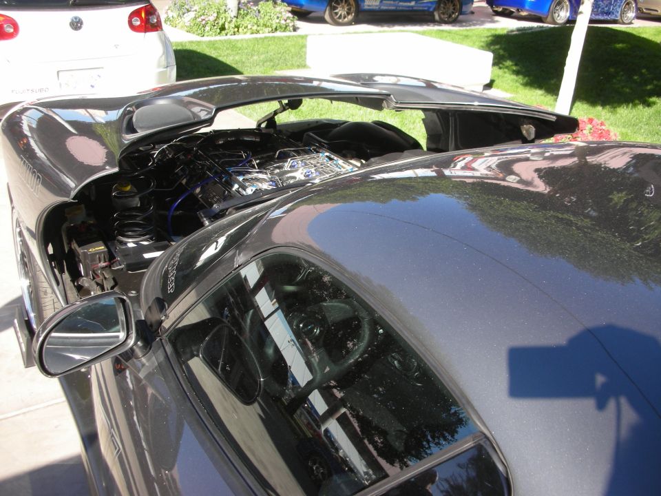 Gray sports car with rear hatch open showing engine in show lot