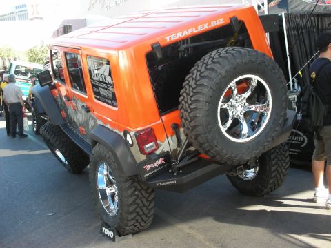 1998 Ford Crown Victoria - orange lifted Jeep Wrangler Unlimited with chrome wheels, oversized tires and a Teraflex.biz windshield decal on display at an outdoor even…