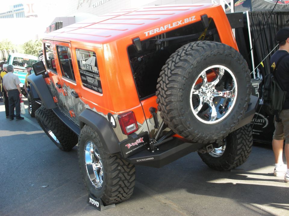 Orange lifted Jeep Wrangler Unlimited with chrome wheels and rear-mounted spare at outdoor show