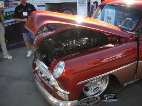 1998 Ford Crown Victoria - candy-orange 1950s custom car shown with its hood open, revealing a polished multi-carburetor V8 engine.