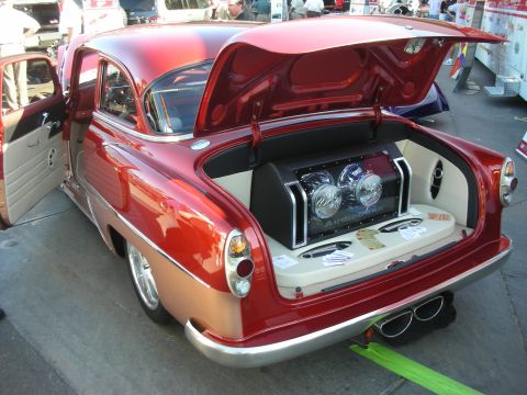 1998 Ford Crown Victoria - red-and-gold two-tone 1950s custom car with its trunk open to reveal a finished audio amplifier and component display.