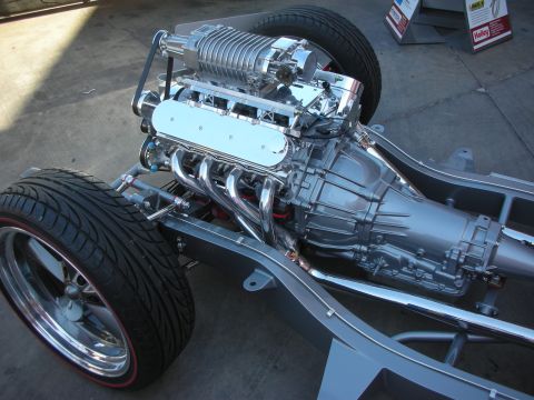 1998 Ford Crown Victoria - polished supercharged V8 engine with long-tube headers mounted on a bare rolling chassis fitted with staggered wheels and tires.