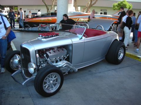 1998 Ford Crown Victoria - silver hot rod roadster with a red interior and an exposed chrome V8 engine parked outdoors among other show cars.