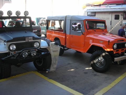 1998 Ford Crown Victoria - orange Toyota Land Cruiser FJ45 pickup with a soft top parked next to a gray Land Cruiser FJ40 at an outdoor show.