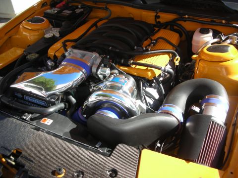 1998 Ford Crown Victoria - Detailed engine bay of an orange vehicle featuring a chrome supercharger, polished intake piping and a red cone air filter.