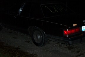 1990 Mercury Grand Marquis - A black sedan is seen from the rear, with the letters "DM" scrawled on the back window.