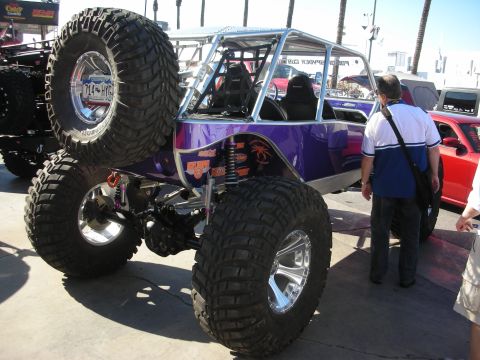 1998 Ford Crown Victoria - purple tube-chassis rock-crawler buggy with oversized mud tires, roll cage and long-travel shocks displayed outdoors.