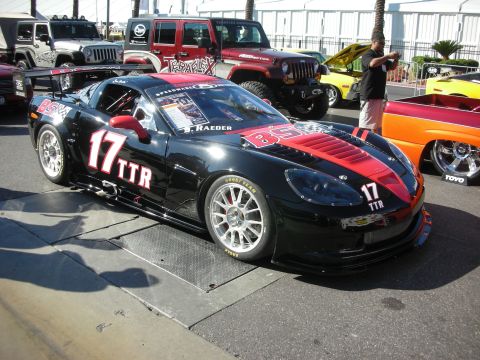 1998 Ford Crown Victoria - black and red Chevrolet Corvette race car numbered 17 TTR with front splitter and racing wheels parked near Jeeps at a show.