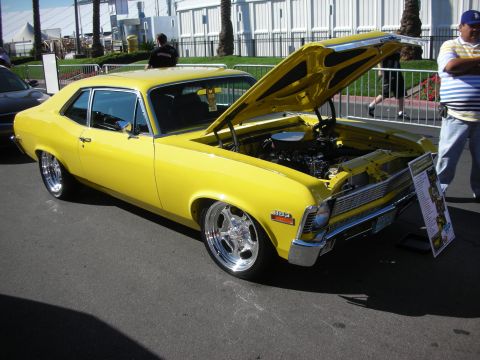 1998 Ford Crown Victoria - yellow Chevrolet Nova coupe with hood raised, chrome five-spoke wheels and a built engine on display at a show.