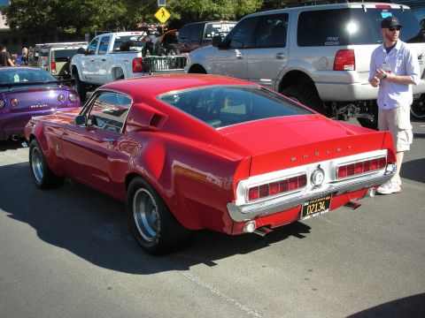 1998 Ford Crown Victoria - Rear three-quarter view of a red Shelby Mustang fastback with chrome rear bumper and slotted wheels in a parking lot show.