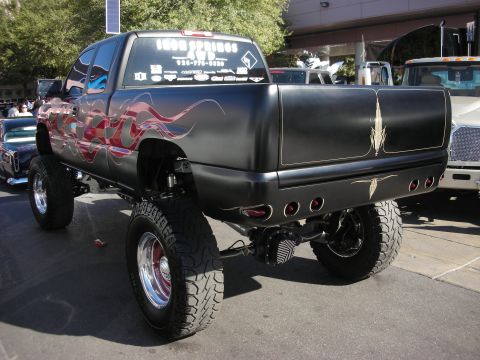 1998 Ford Crown Victoria - Rear view of a lifted black pickup with red flame graphics, chrome wheels and oversized tires at an outdoor event.