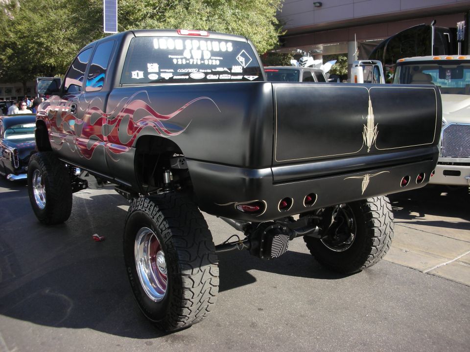 Lifted black GMC or Chevy pickup with red flame graphics and chrome wheels, rear view