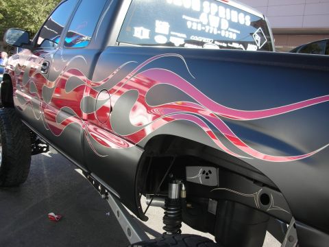 1998 Ford Crown Victoria - Detail of a black pickup's bed side showing elaborate red and purple flame airbrush graphics over matte paint.