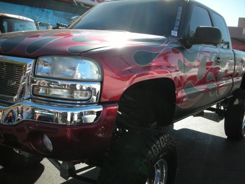 1998 Ford Crown Victoria - Front three-quarter view of a lifted maroon GMC Sierra pickup with gray flame graphics, chrome bumper and large off-road tires.