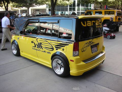 1998 Ford Crown Victoria - lowered yellow boxy compact wagon with custom black graphics and chrome wheels parked at an outdoor show.