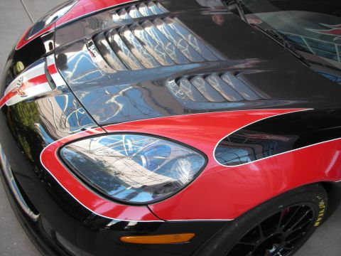 1998 Ford Crown Victoria - Detail of a black sports car's front fender showing red accent graphics, a headlight, hood vents, and a black wheel.