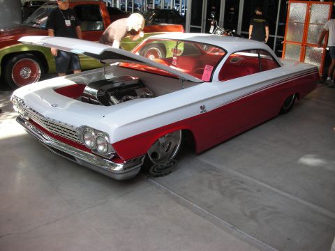 1998 Ford Crown Victoria - white-over-red lowered classic two-door hardtop sits with its hood open among other cars at an indoor show.