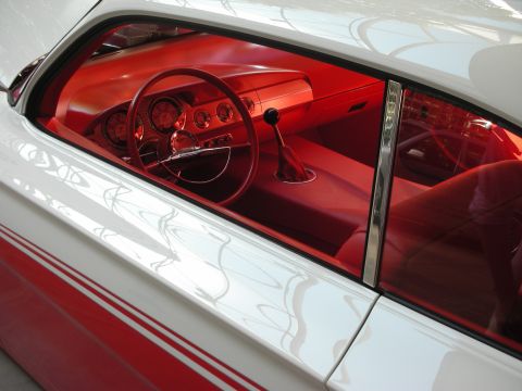 1998 Ford Crown Victoria - Through a side window, a classic car's bright red interior shows a dished steering wheel, dash gauges, and floor shifter.