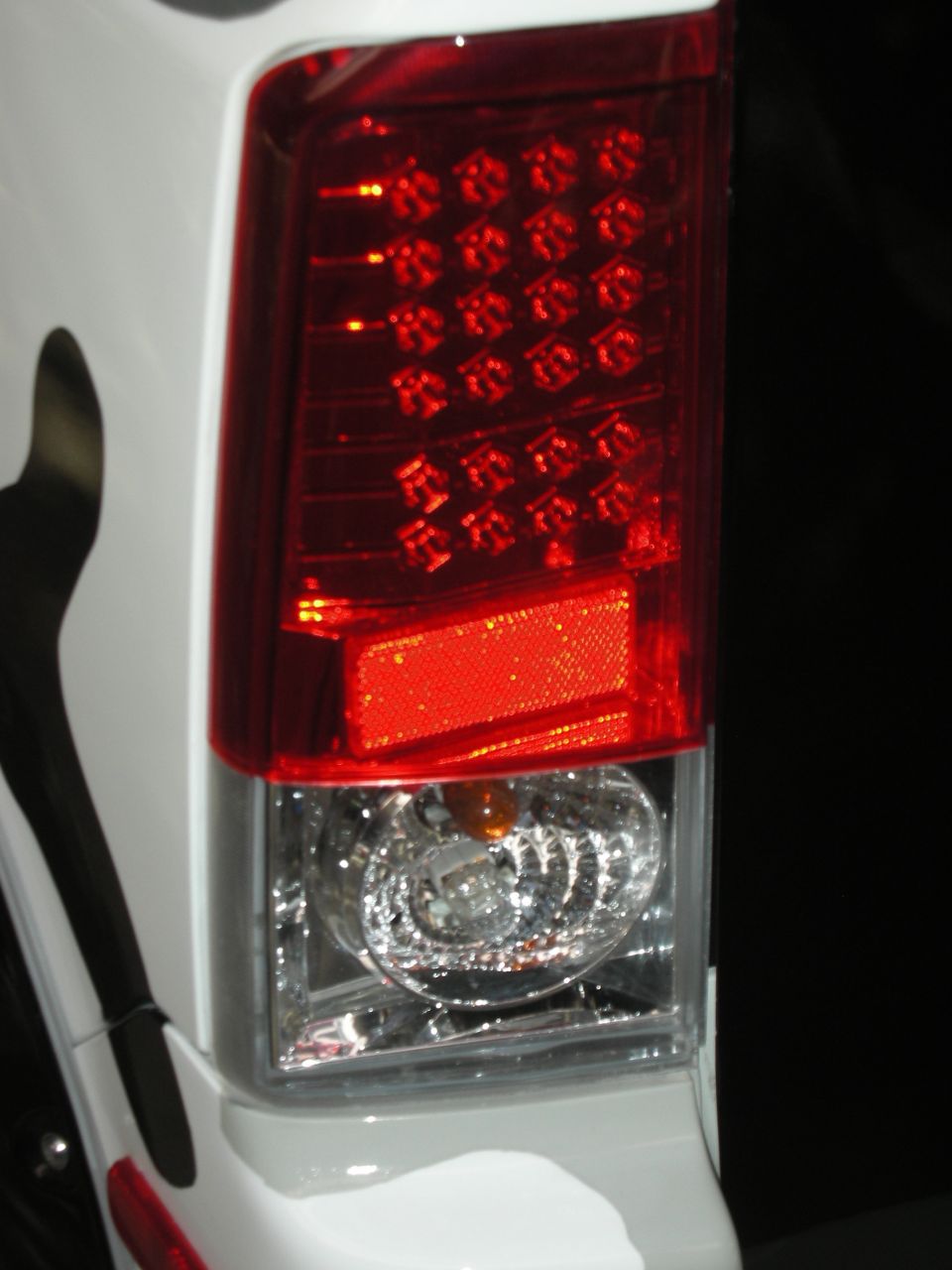 Close-up of a red and clear LED taillight on a white vehicle body