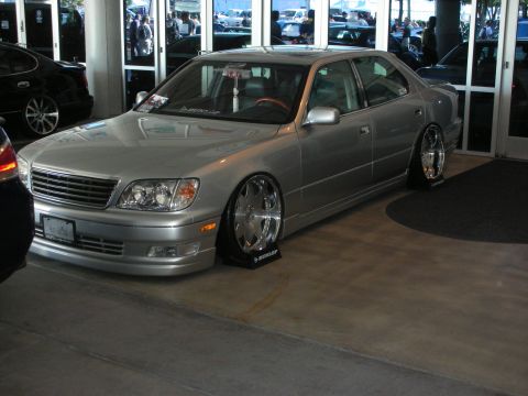 1998 Ford Crown Victoria - silver lowered luxury sedan on polished chrome wheels with Dunlop tire markers sits indoors at a show.