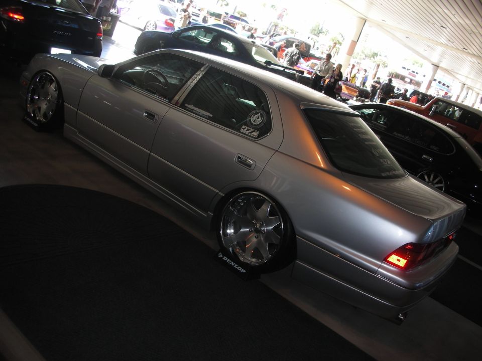 Silver lowered luxury sedan on chrome wheels from rear quarter at indoor show