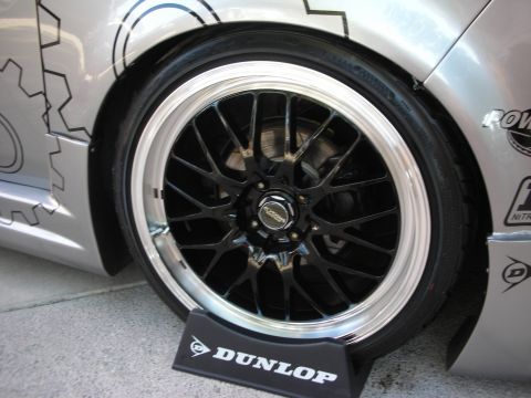 1998 Ford Crown Victoria - black multi-spoke wheel with a polished lip on a silver car, with a Dunlop tire marker on the ground beneath it.