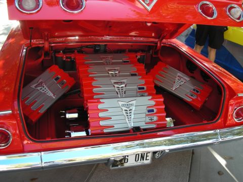 1998 Ford Crown Victoria - red classic car's open trunk is filled with a symmetrical array of gray car-audio amplifiers above a '6 ONE' plate.
